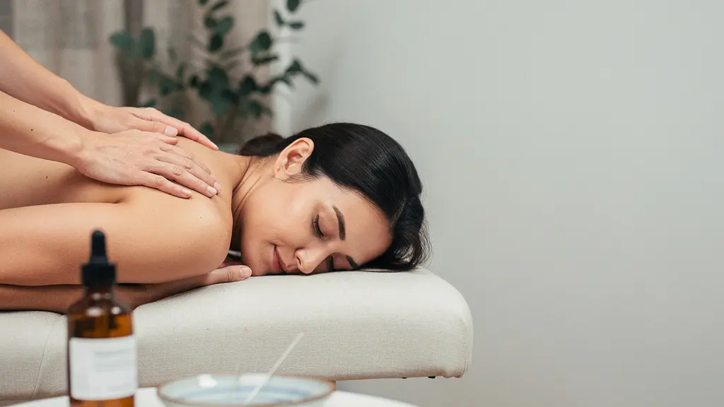 Un praticien réalise une manipulation douce de l’épaule d’un patient dans un cabinet apaisant, avec un flacon d’huile de CBD non identifiable au premier plan et un large espace vide sur le côté.