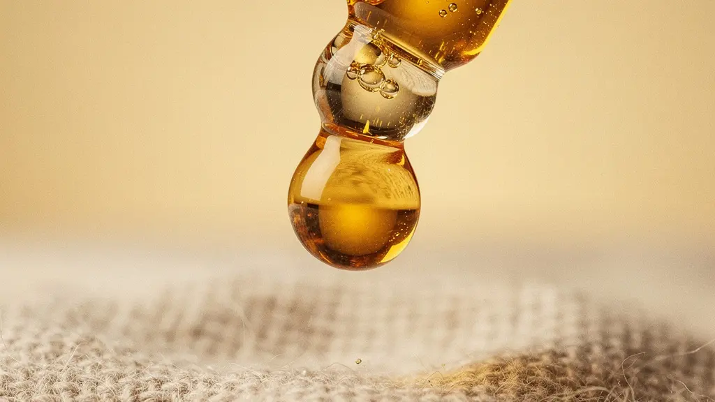 Gros plan macro sur un compte-gouttes en verre libérant une goutte d'huile dorée dans la lumière du matin, avec une texture de grain subtile