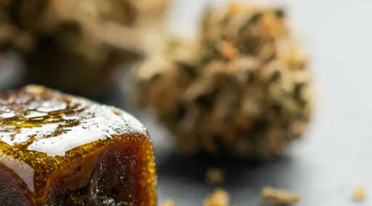 Bloc de résine CBD artisanale posé sur une surface en pierre naturelle, éclairé par une lumière dorée révélant sa texture grasse et ses reflets ambrés