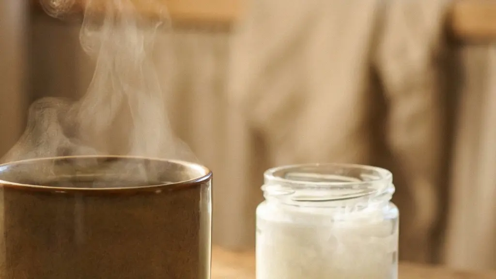 Tasse fumante d'infusion au CBD posée près d'une cuillère d'huile de coco et de fleurs de chanvre séchées, dans une lumière dorée naturelle