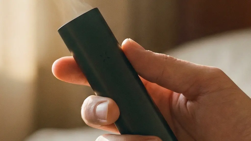 Main tenant délicatement un vaporisateur portable dans une atmosphère apaisante de lumière tamisée, vapeur légère s'élevant dans un rayon de soleil